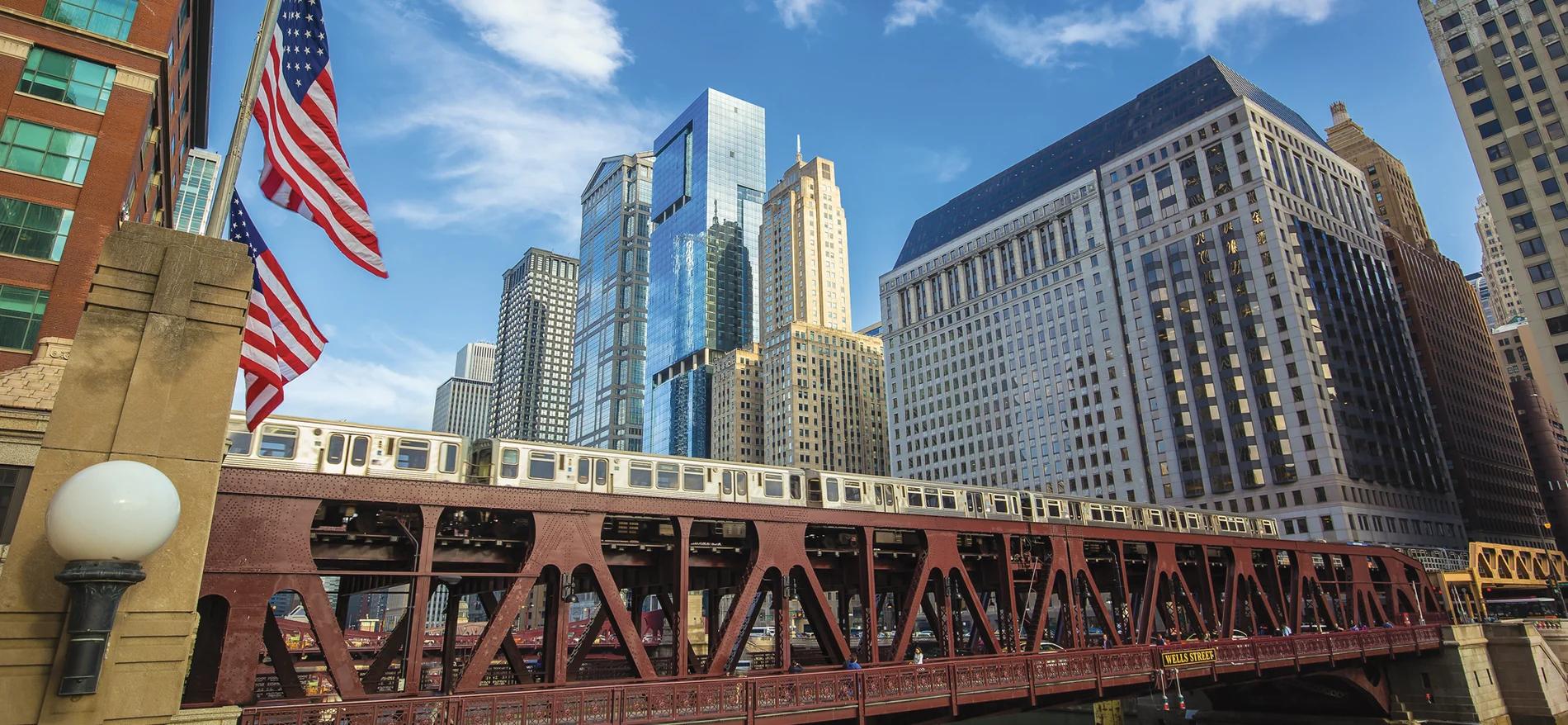 Downtown Chicago — an elevated train crossing the Wells Street bridge, with American flags and the Loop skyline