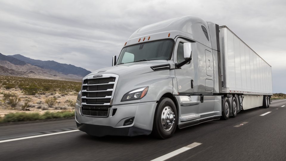 Silver Freightliner Cascadia semi truck with trailer driving on a desert highway