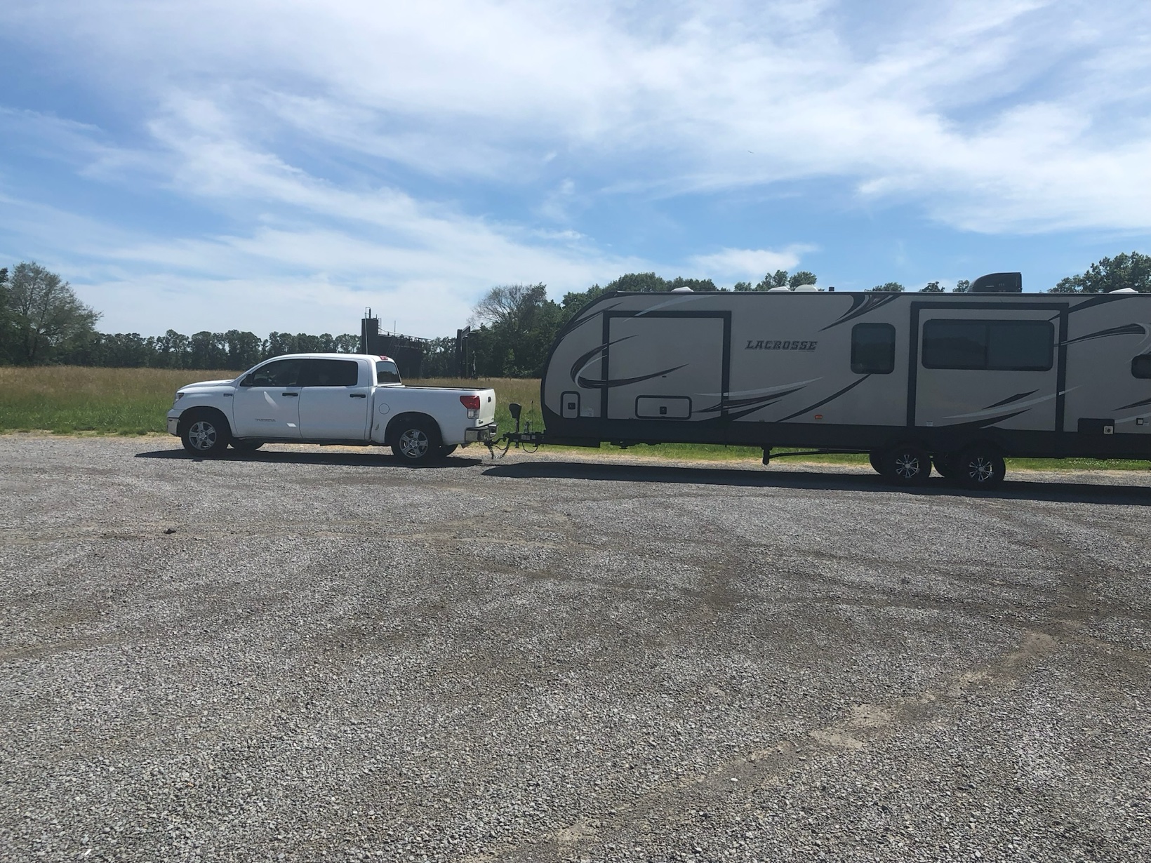 Side view of the white pickup truck towing a Lacrosse travel trailer on a gravel lot