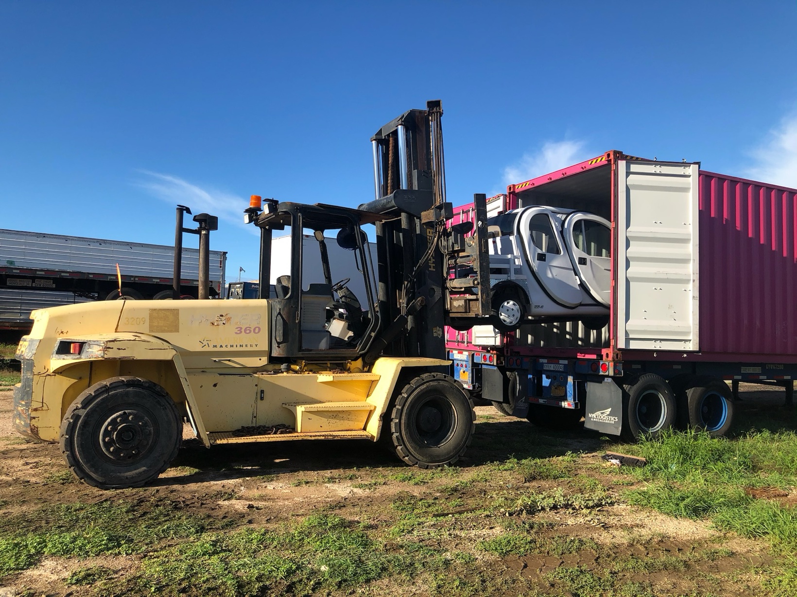 Large forklift loading a small vehicle into a shipping container