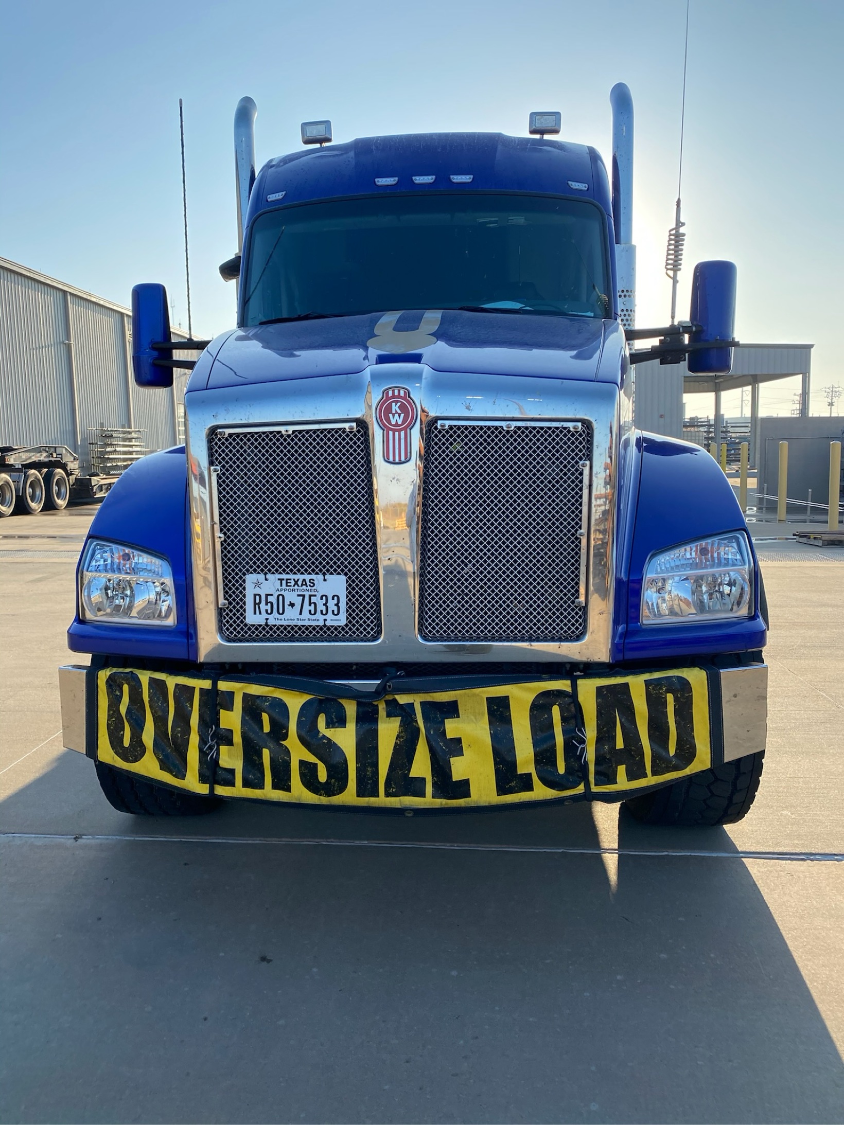 Blue Kenworth semi truck with an OVERSIZE LOAD banner, front view