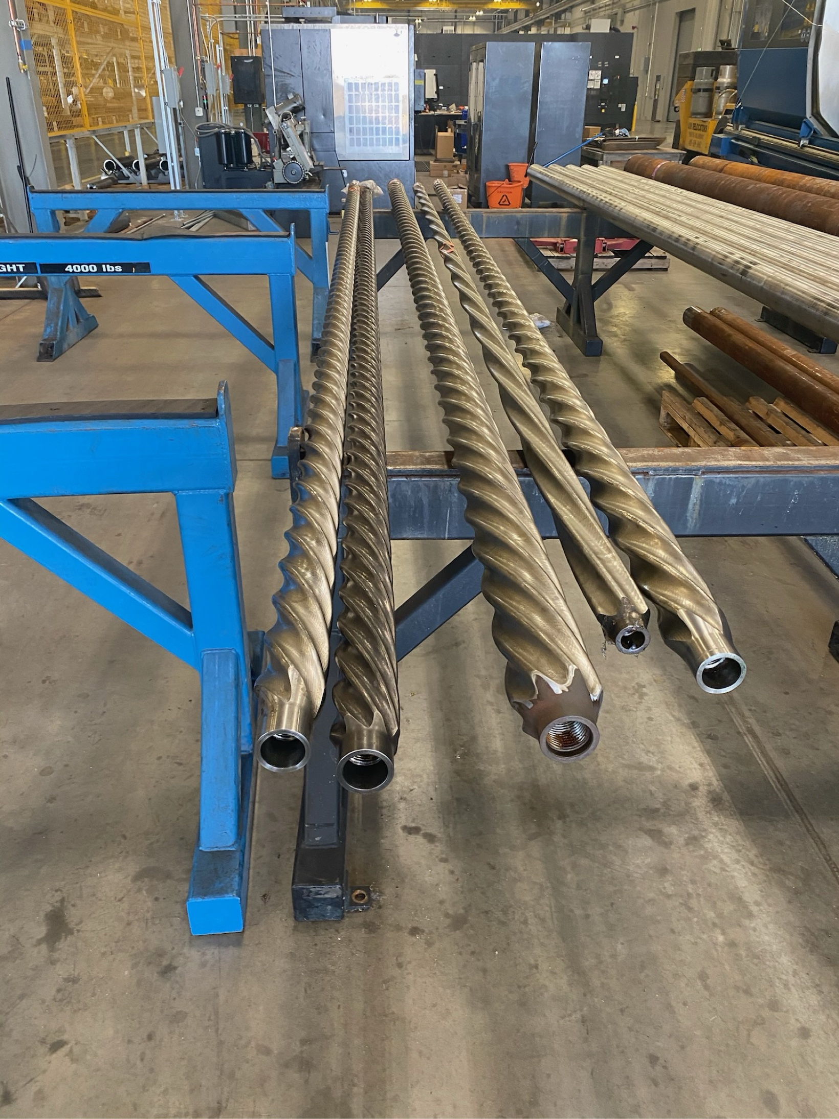 Long helical drilling shafts on racks in a workshop